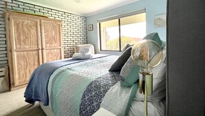 Een slaapkamer met een bed, een plafondventilator, een raam, een bakstenen muur en een kledingkast.