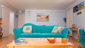 Een woonkamer met een turquoise bank, een houten salontafel en een schilderij aan de muur.