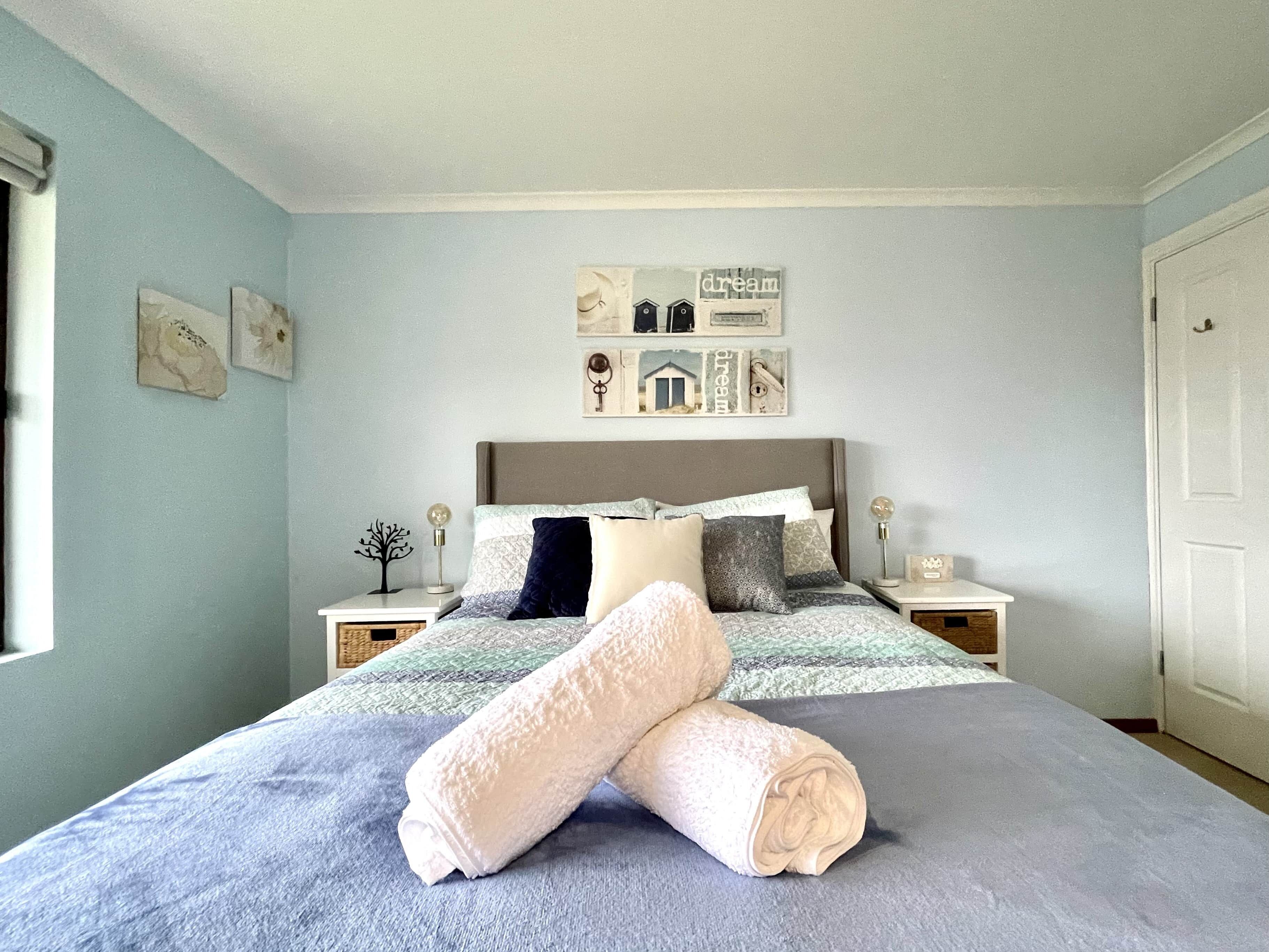 A neatly made bed with rolled towels, a headboard, and a wall with framed pictures.