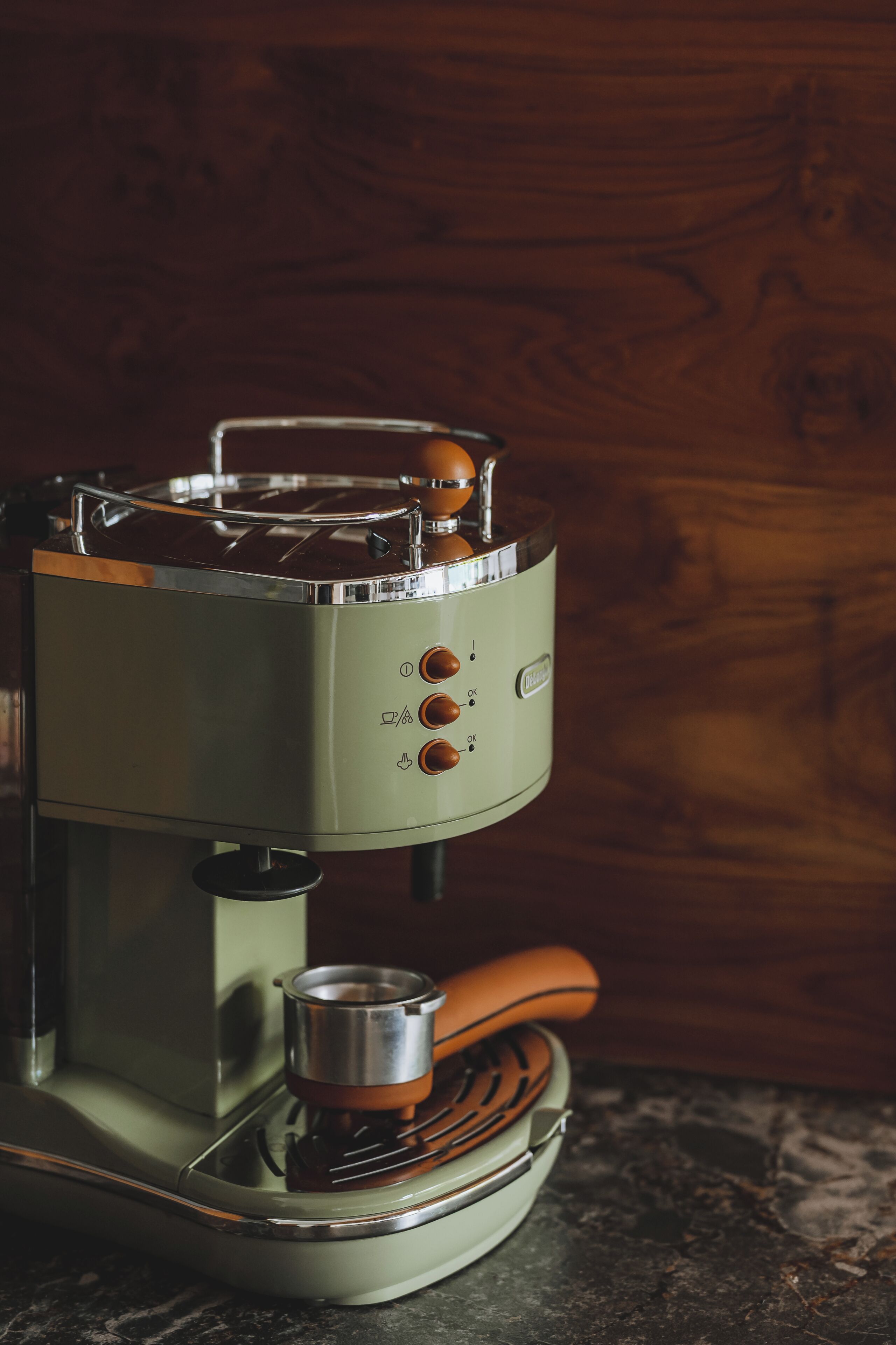 A vintage espresso machine with a metal container on top, a control panel with buttons, and a wooden spoon inside.