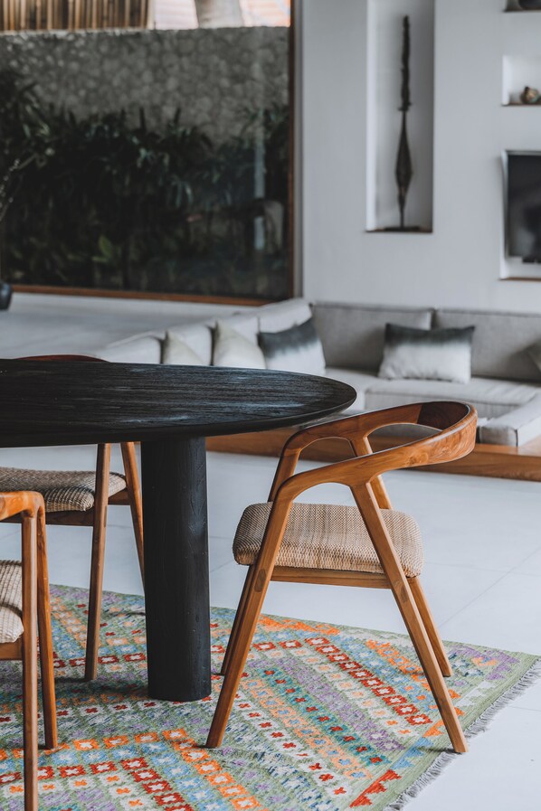 A dining area with a round table, wooden chairs, a patterned rug, and a sofa in the background. - Villa Caz a Bali (Canggu)