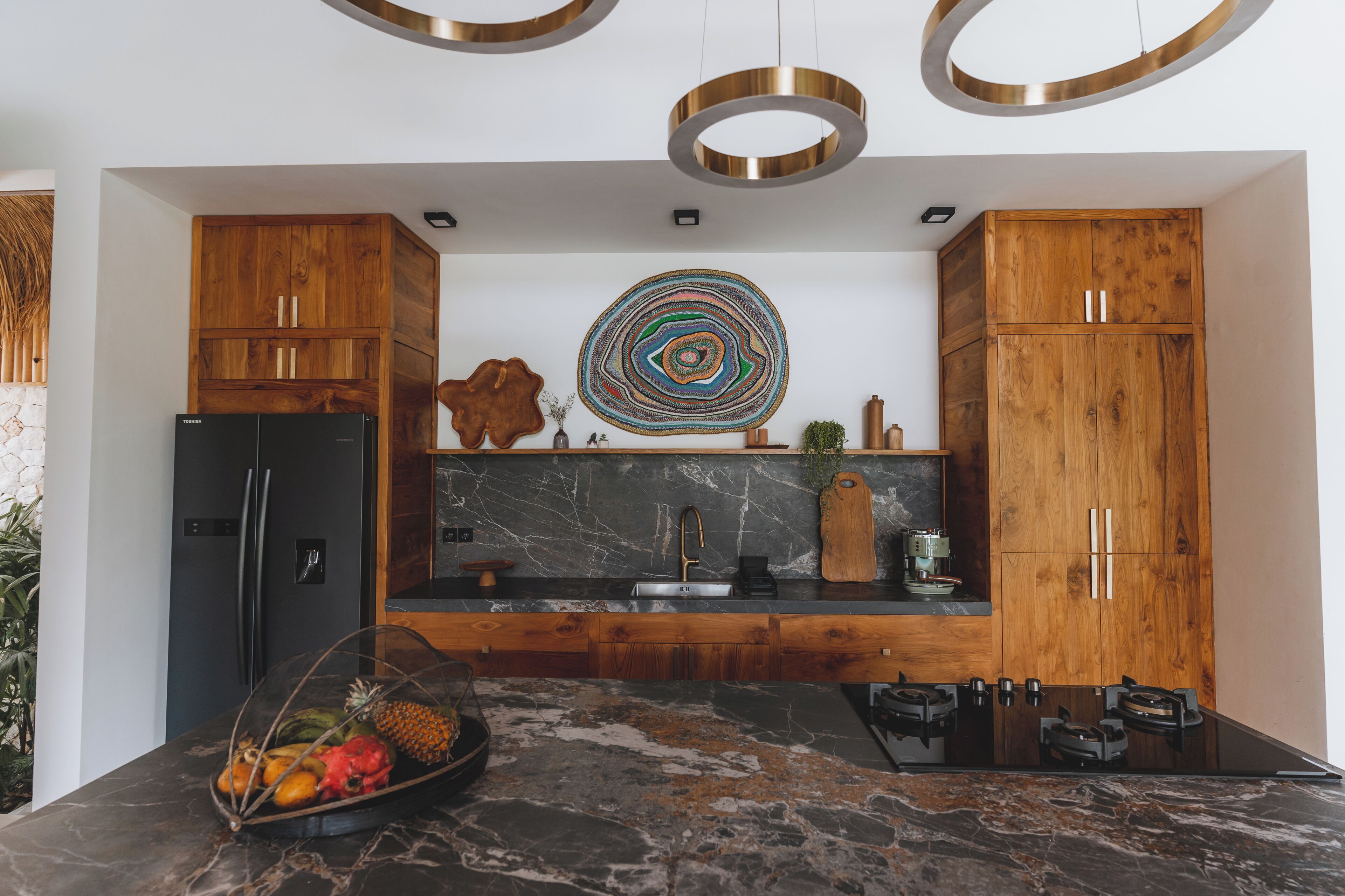 Een moderne keuken met houten kastjes, een zwarte koelkast, een marmeren aanrechtblad en een opvallend rond kunstwerk aan de muur.