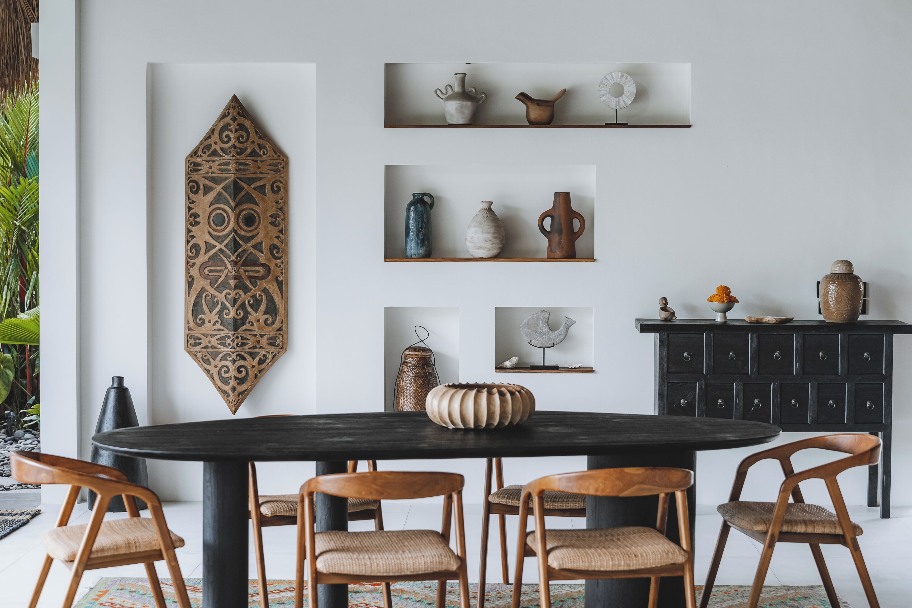 A dining area with a round table, six wooden chairs, and shelves with decorative items.