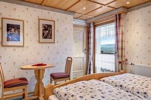 Ein Zimmer mit zwei Betten, einem kleinen Tisch, einem Stuhl und einem Fenster mit Vorhängen.