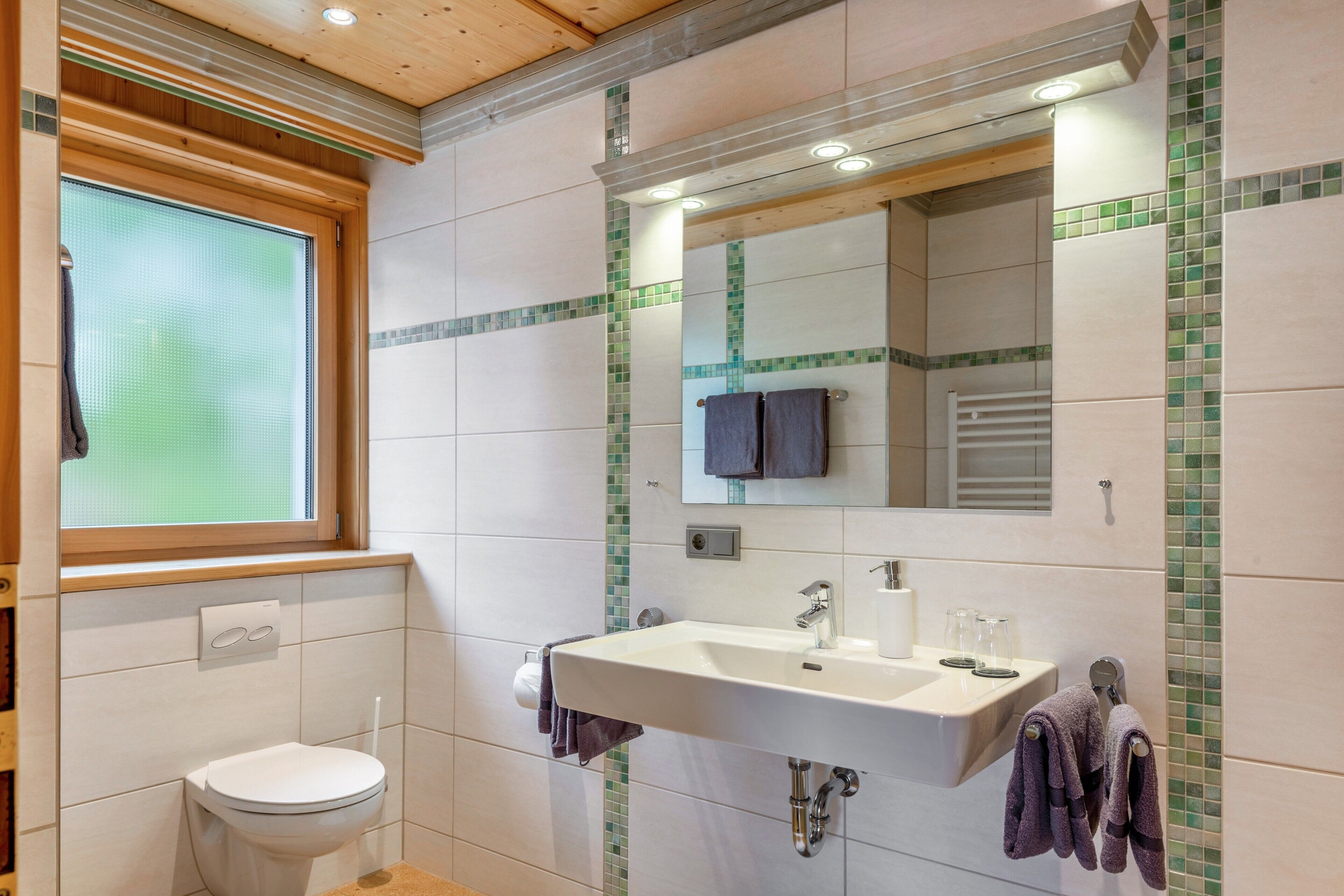 A bathroom with a toilet, sink, mirror, and window.