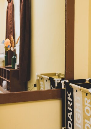 Une salle de bain avec un miroir, un porte-serviettes et une étagère où sont posées des bouteilles et des fleurs.