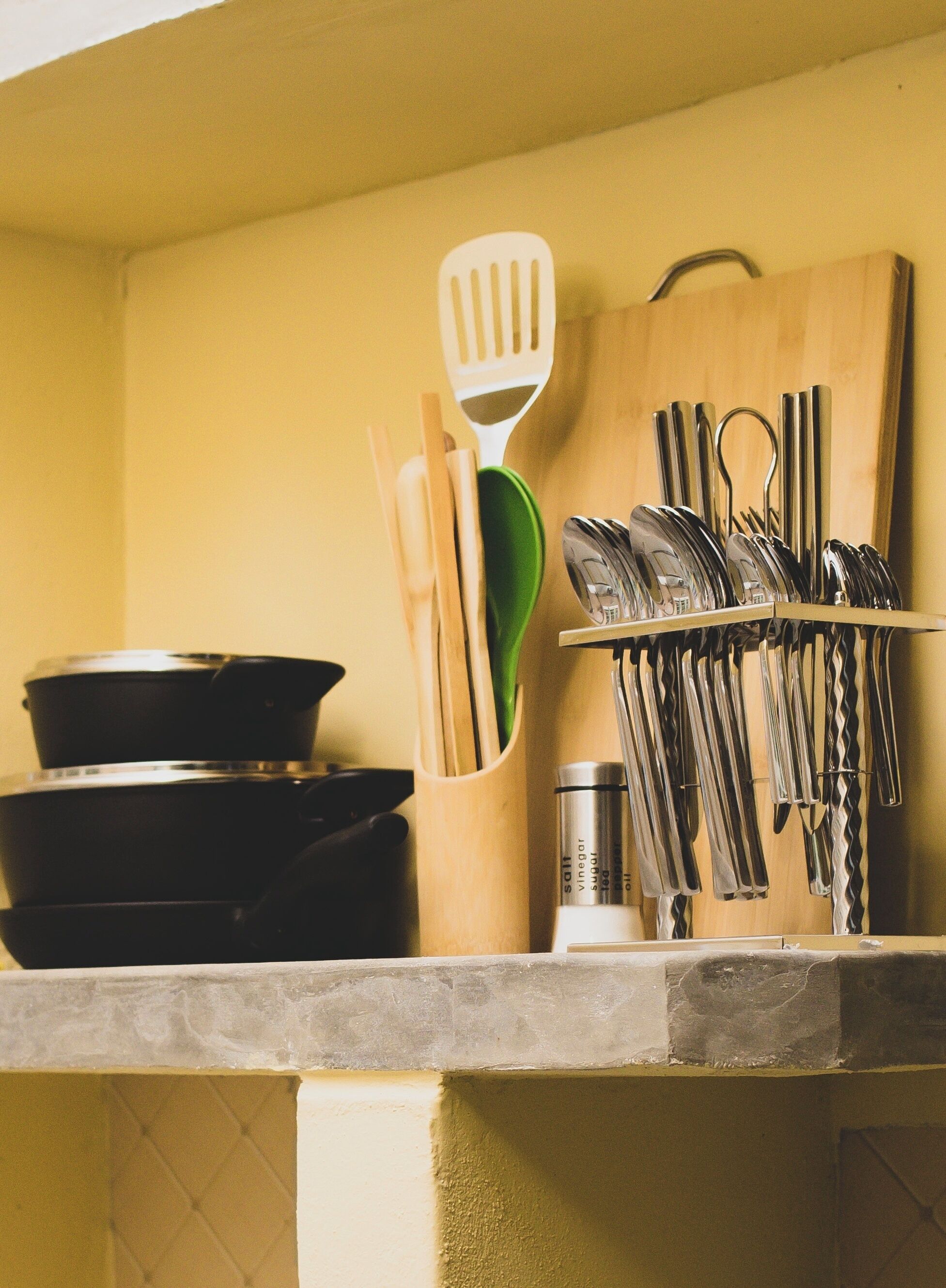 A kitchen counter with a pot, a spatula, a knife block, and a bottle of salt, vinegar, sugar, and oil.