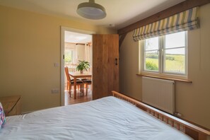 Une chambre avec un grand lit, une porte en bois, une fenêtre avec des stores et une vue sur un coin repas.