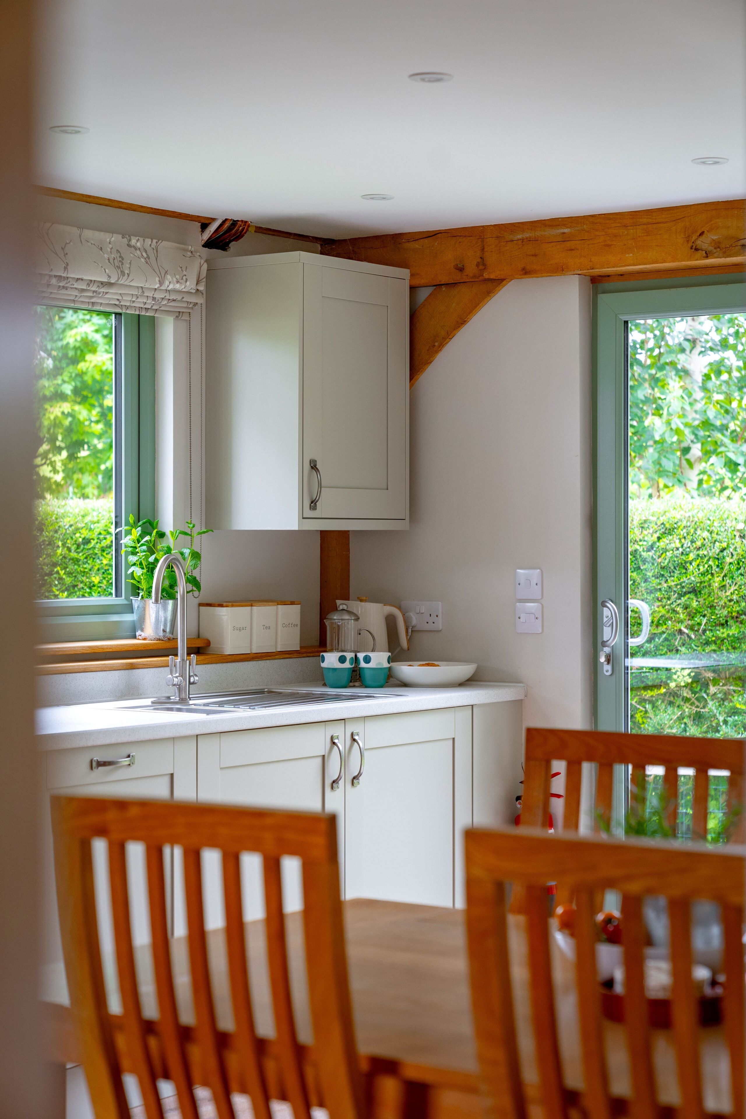 Une cuisine avec des meubles blancs, un plafond en bois et une fenêtre donnant sur un paysage verdoyant.
