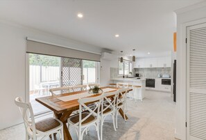 A modern kitchen with white cabinets, a wooden dining table, and white chairs. - Sandy Shores by Ready Set Stay (Tootgarook)