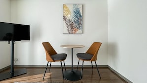 Quarto moderno com televisão de tela plana, duas cadeiras, uma mesa redonda e um quadro abstrato colorido na parede.