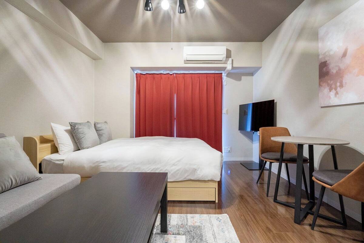 A bedroom with a bed, a sofa, a table, and a TV.