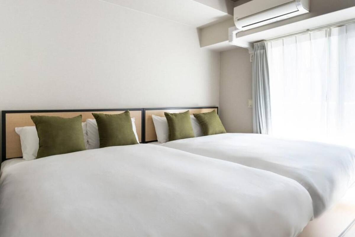 A hotel room with two beds, a headboard, an air conditioning unit, and a window with curtains.