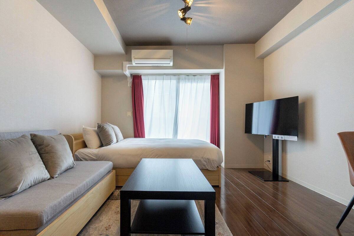A modern hotel room with a bed, sofa, TV, and an air conditioning unit.