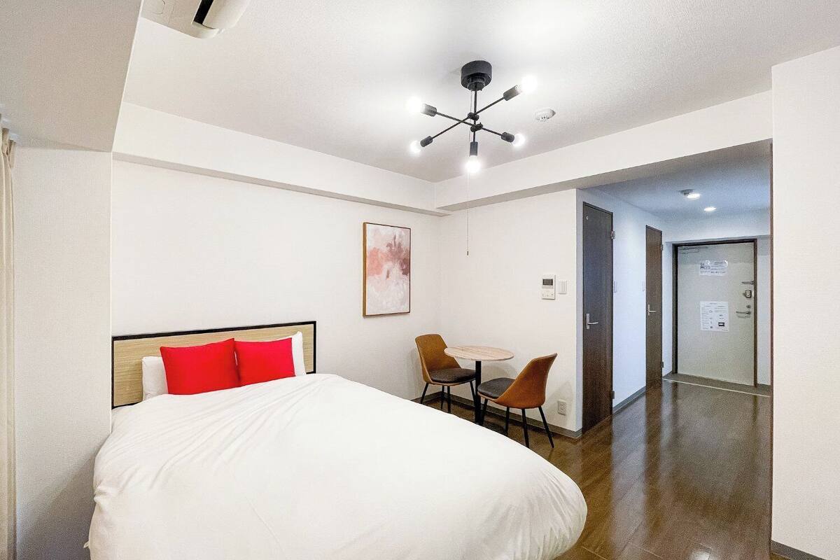 A hotel room with a bed, a desk, two chairs, a ceiling light fixture, and a door.