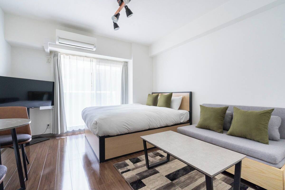 A modern hotel room with a bed, sofa, TV, and a small table.