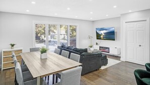 A modern living room with a dining table, grey sofas, and a TV mounted on the wall. - Luxury Estate+Renovated 3 BD+65" TV+WFH+Sleeps 9 (Kitchener)