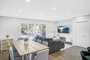 Ein modernes Wohnzimmer mit Esstisch, grauen Sofas und einem an der Wand befestigten Fernseher.