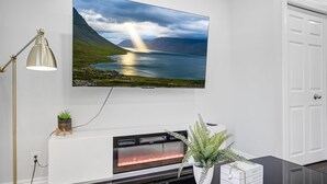 A modern living room with a fireplace, a mounted TV, and a potted plant. - Luxury Estate+Renovated 3 BD+65" TV+WFH+Sleeps 9 (Kitchener)