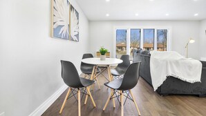 A dining area with a round table, black chairs, and a grey sofa with a white throw. - Luxury Estate+Renovated 3 BD+65" TV+WFH+Sleeps 9 (Kitchener)