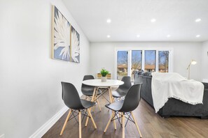 Ein Essbereich mit einem runden Tisch, schwarzen Stühlen und einem grauen Sofa mit weißer Decke.