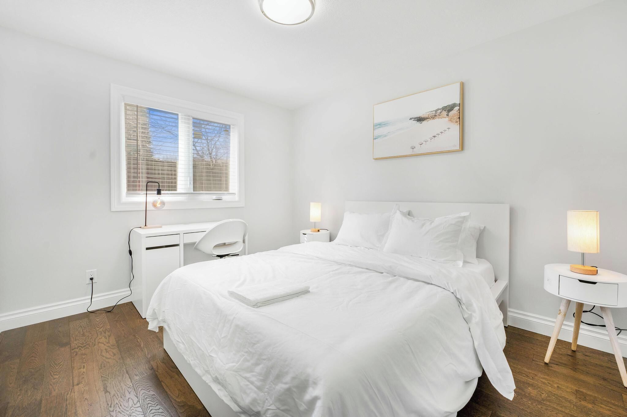 A bedroom with a bed, bedside lamps, a desk, and a window.