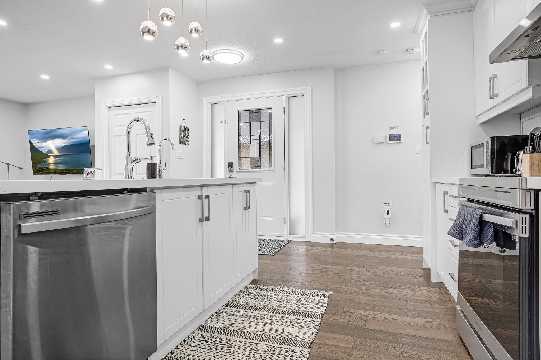 A modern kitchen with stainless steel appliances, white cabinetry, and a wooden floor.