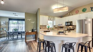 A modern kitchen with a central island, bar stools, and a dining area with a table and chairs. - Patio & Poolside Relaxation! Palm Coast Getaway (Palm Coast)