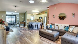 A spacious living area with a kitchen, a dining area, and a large round mirror on the wall. - Patio & Poolside Relaxation! Palm Coast Getaway (Palm Coast)