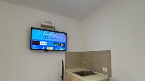 Uma cozinha compacta com máquina de lavar louça embutida, pia e televisão na parede exibindo a interface de um serviço de streaming.