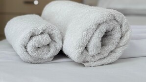 Uma toalha branca e bem dobrada sobre uma cama em um quarto de hotel.