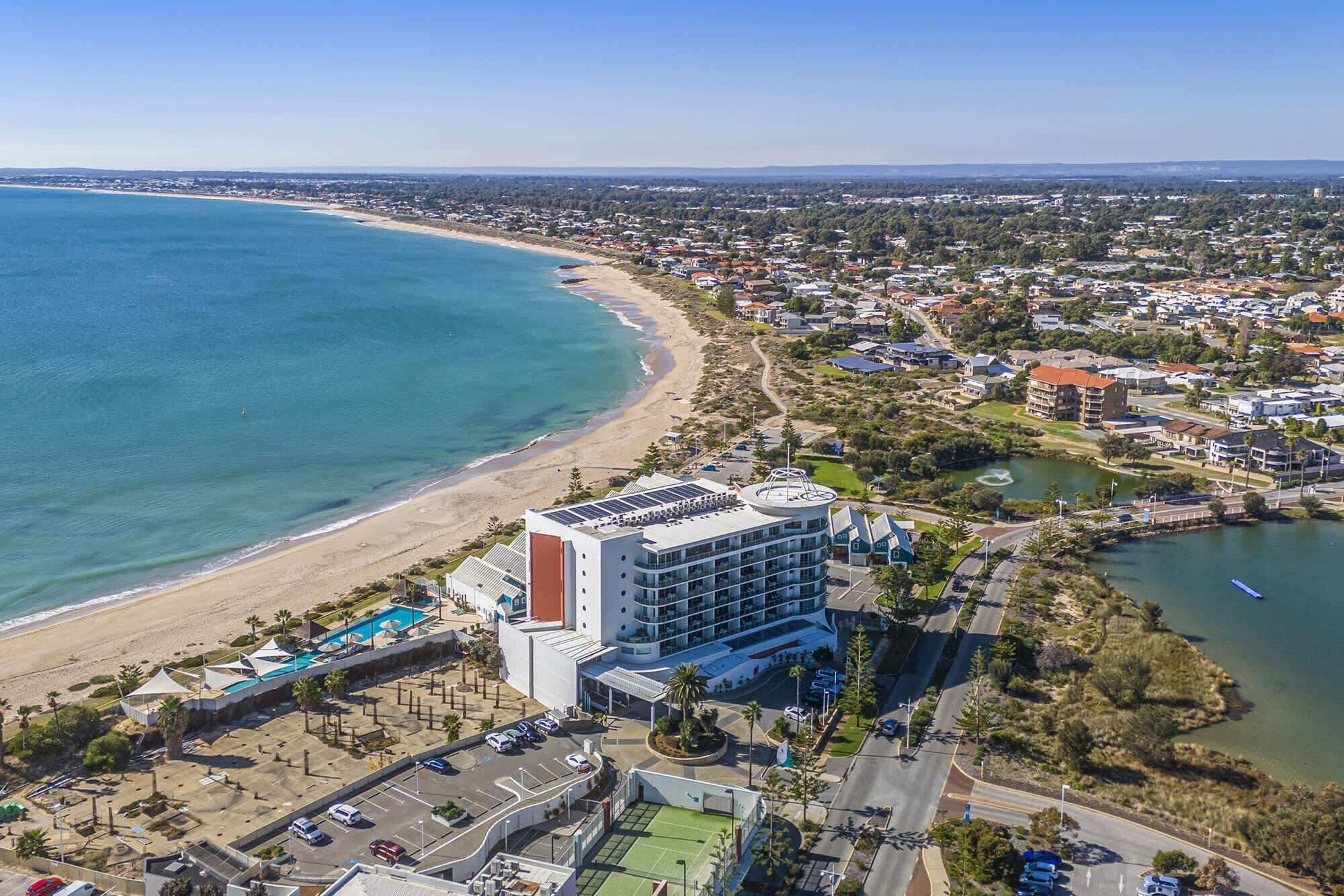 A coastal hotel with a pool, tennis court, and a view of the beach and ocean.