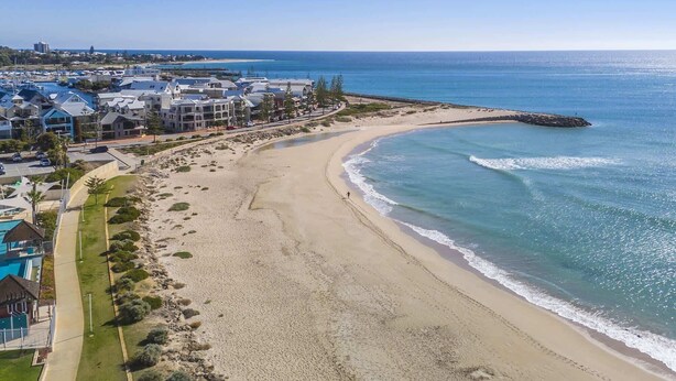 A coastal residential area with beachfront properties, a curved sandy beach, and a rocky outcrop in the water. - Coastal Studio | City & Ocean Views, Walk to Beach (Mandurah)
