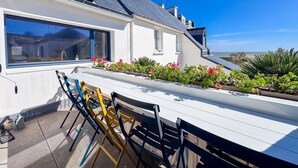 A modern house with a balcony, a dining area with chairs, and a view of the sea.