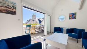 A modern living room with a large window, a dining area, and a view of a building with a sloped roof.