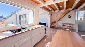 A modern kitchen with a large window, wooden ceiling beams, and a dining area with a table and chairs.