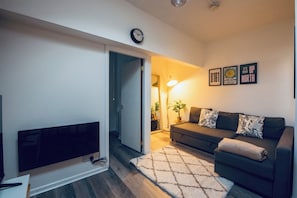 Uma sala de estar com televisão de tela plana, sofá, tapete e relógio de parede.
