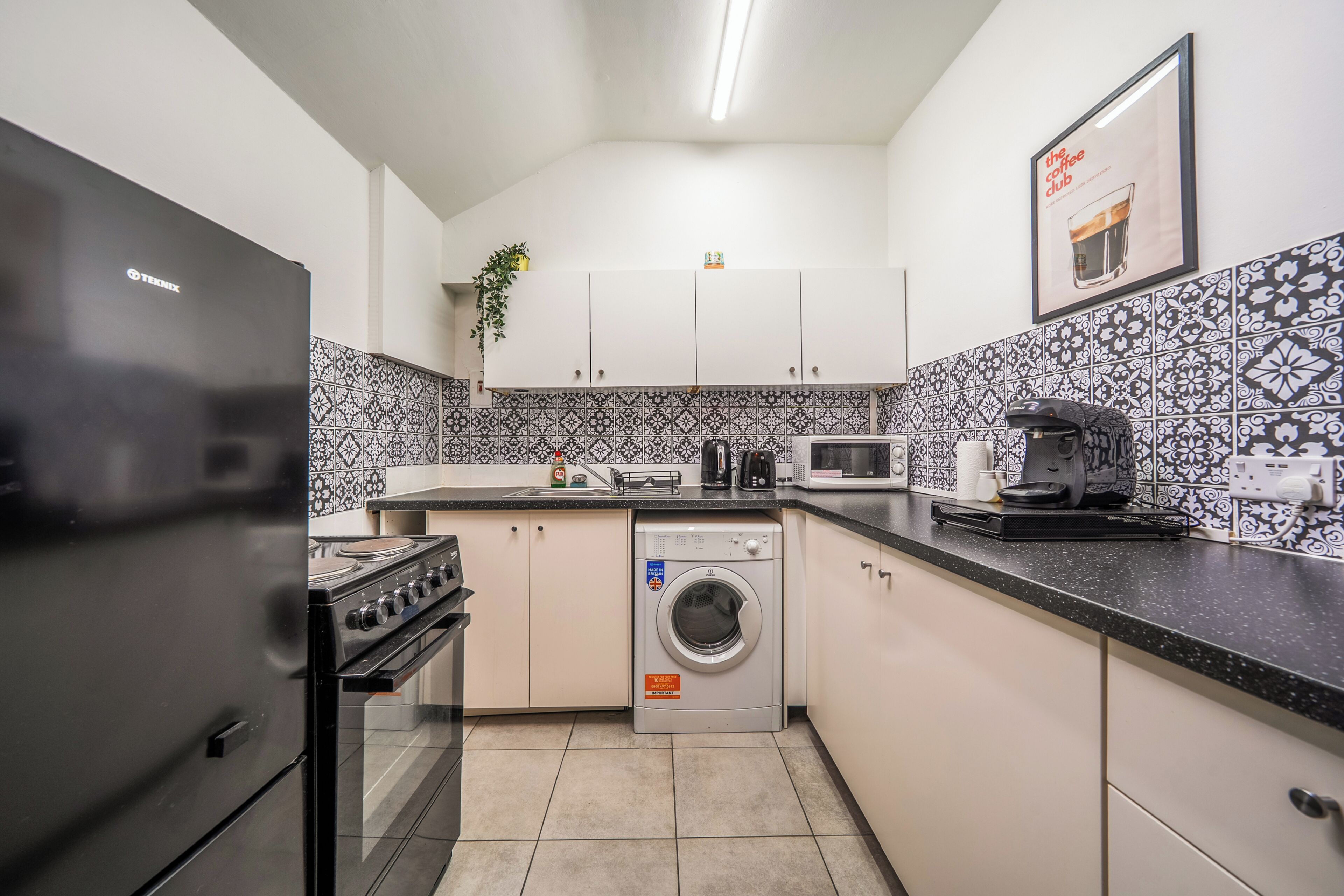 A compact kitchen with a refrigerator, stove, microwave, and washing machine.