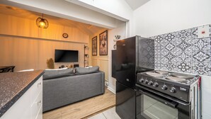 A modern kitchen with a black refrigerator, a stove, and a flat-screen TV mounted on the wall. - Apartment in Cite Center (Manchester)
