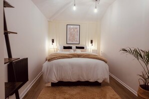 Une chambre à coucher avec un lit, des lampes de chevet, un tableau encadré au mur, un radiateur et une plante en pot.
