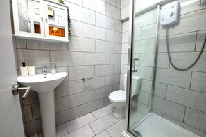Une salle de bain avec un lavabo blanc, des toilettes et une douche fermée par des parois en verre.