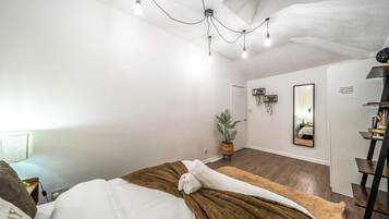 A hotel room with a bed, a bedside table, a mirror, a potted plant, and a door.