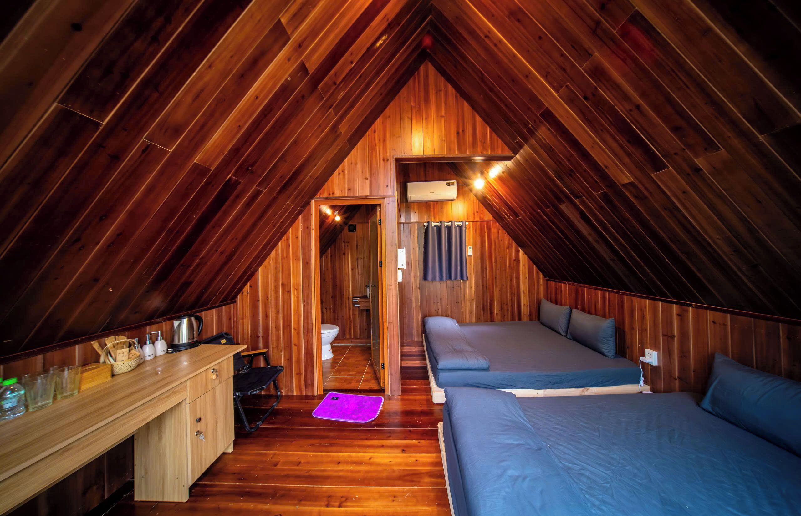 Ein gemütliches Schlafzimmer im Dachgeschoss mit Holzwänden, einem Schreibtisch mit Stuhl, zwei Betten und einem durch eine Tür erreichbaren Badezimmer.