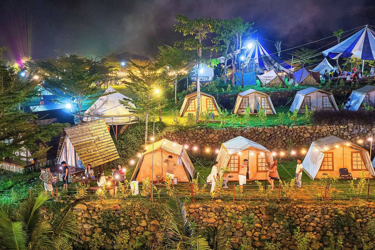 A series of tents with a stone wall and greenery in the foreground.