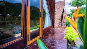 A wooden-framed glass door leading to a garden with a pond, surrounded by tropical plants and a mountain backdrop. - LEAF VILLAGE & FARM LÀNG LÁ (Da Nang)