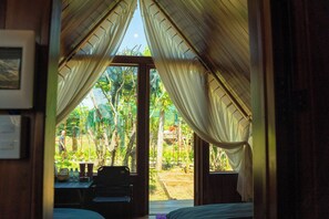 Una habitación con cama, una mesa con objetos y vistas a un jardín a través de cortinas.