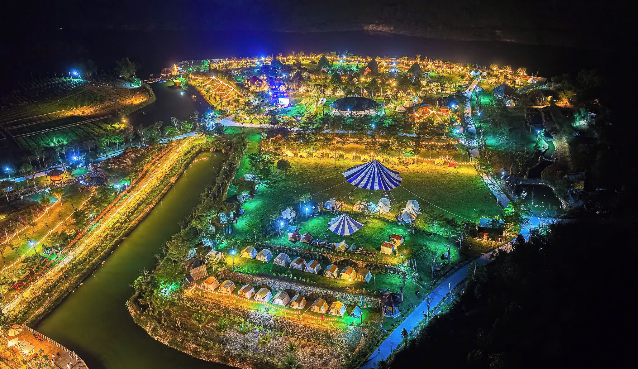 Zona luminosa de un resort con varias tiendas de campaña y una estructura central con techo a rayas.