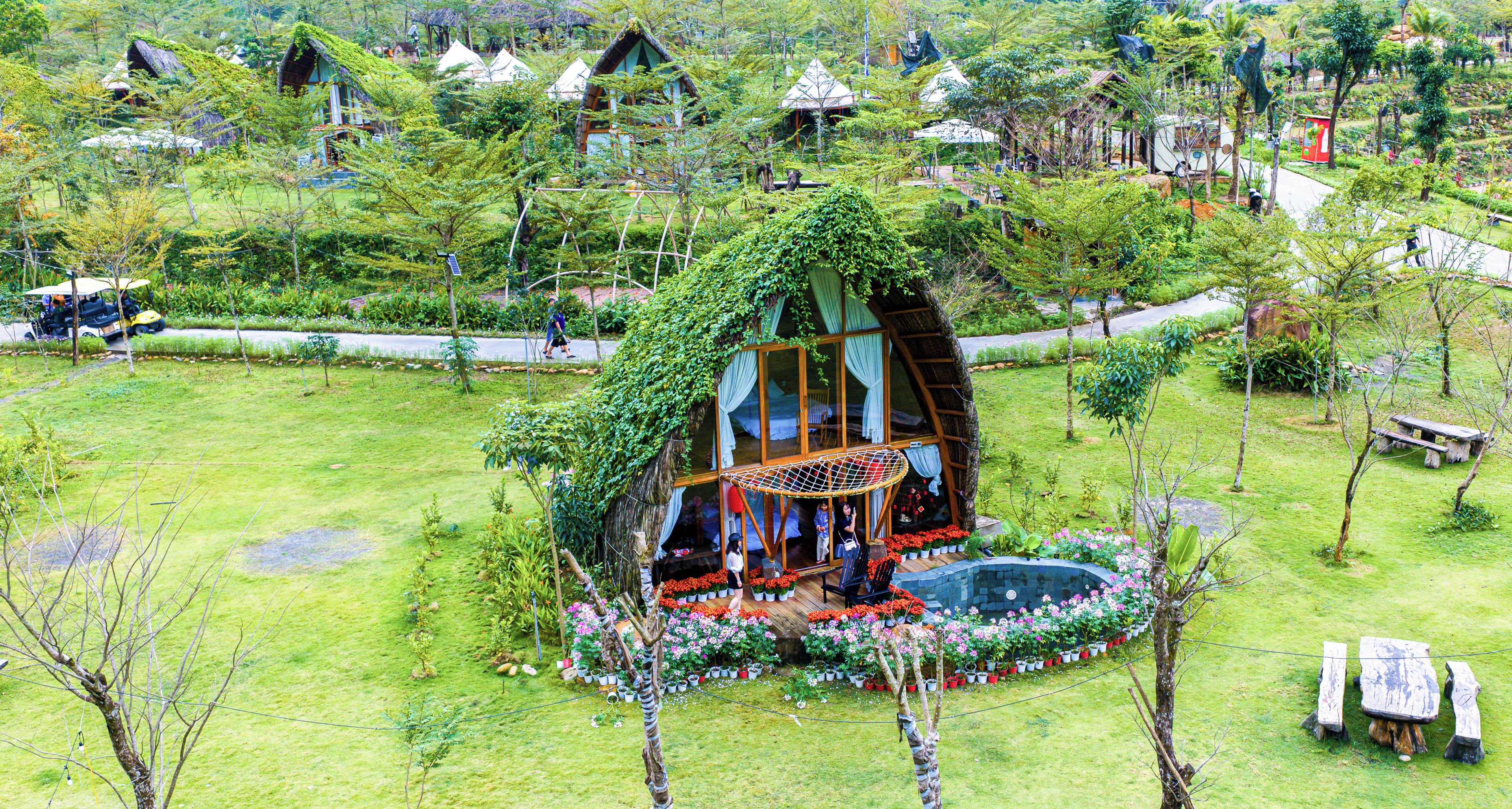 Una casa en el árbol con cerramiento de vidrio, rodeada por un jardín con plantas en macetas y flores.