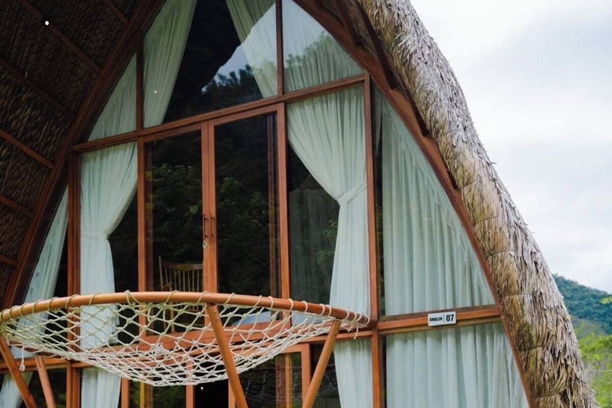 A woman sitting in a pool with a net hoop, a large window, and a thatched roof structure.