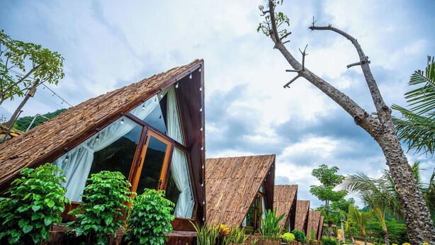 A series of wooden-roofed cabins with large windows, surrounded by lush greenery and a clear sky. - LEAF VILLAGE & FARM LÀNG LÁ (Da Nang)